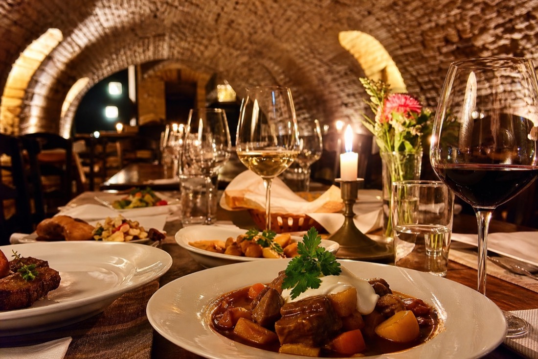 Hungarian dishes and wine glasses by candlelight in a vaulted Budapest cellar during the culinary and wine walk